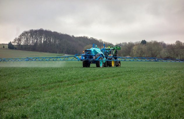 Trator e pulverizador agrícola em campo verde, com névoa de pulverização.