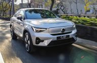 Volvo C40 Recharge prateado em movimento em uma rua urbana ensolarada.