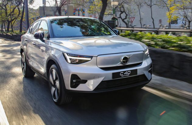 Volvo C40 Recharge prateado em movimento em uma rua urbana ensolarada.