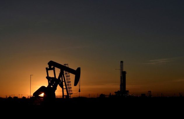 Silhuetas de bomba de petróleo e plataforma de perfuração em campo industrial ao pôr do sol.