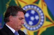 Jair Bolsonaro, de perfil, olhando para baixo, com a bandeira do Brasil desfocada atrás.