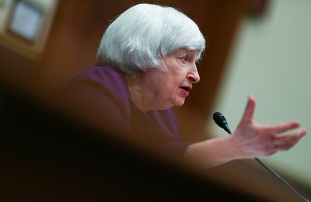 Mulher de cabelo branco, vestindo roxo, fala ao microfone e gesticula com a mão, em perfil.