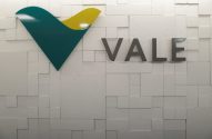 Logotipo da VALE em verde e amarelo e nome "VALE" em cinza, sobre uma parede branca texturizada com blocos.