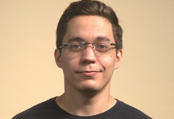 Retrato de homem jovem com óculos e camiseta preta, sorrindo levemente para a câmera.