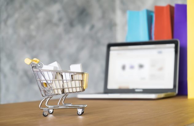 Compras online: carrinho com caixas, laptop e sacolas de compras coloridas.