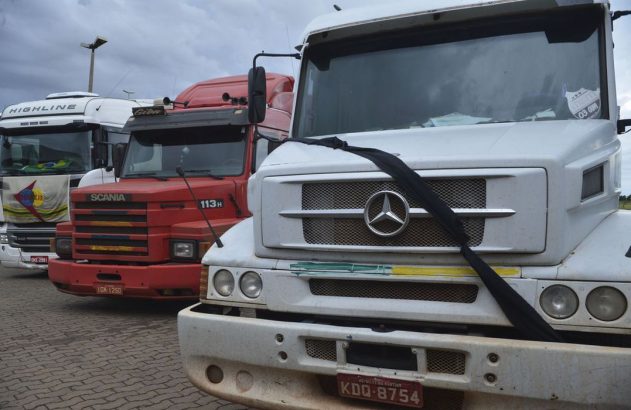 Caminhões estacionados. O branco Mercedes-Benz em primeiro plano exibe uma faixa preta na grade frontal.