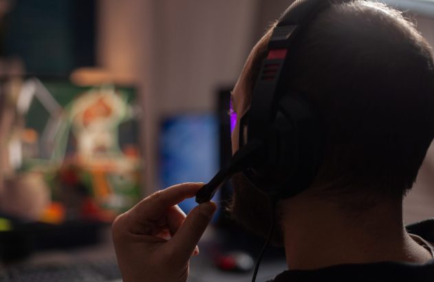 Pessoa usando headset, ajustando o microfone. Telas desfocadas no fundo.