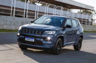 Jeep Compass azul escuro SUV em movimento em pista de corrida com barreiras cinzas ao fundo.