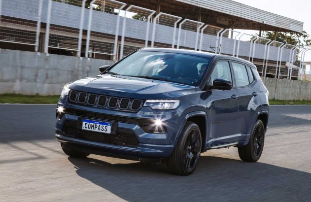 Jeep Compass azul escuro SUV em movimento em pista de corrida com barreiras cinzas ao fundo.
