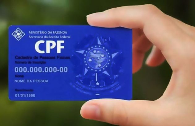 Mão segura cartão CPF azul brasileiro com nome e data de nascimento fictícios.