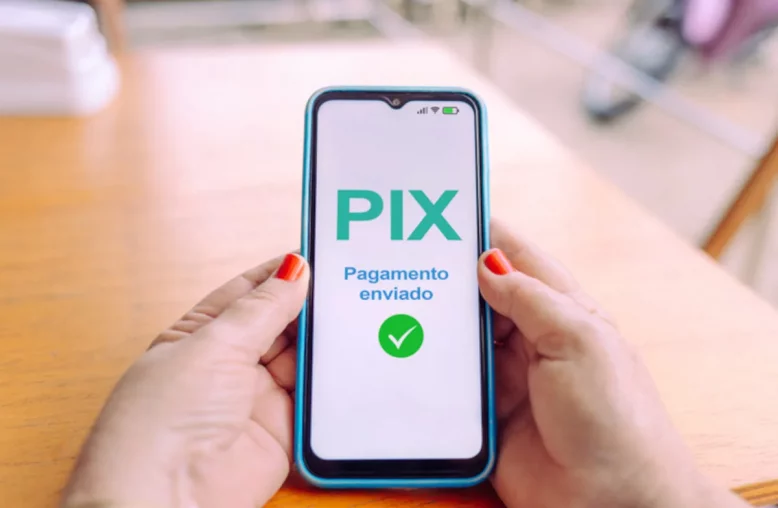 uma mulher segurando um celular com as duas mãos, mostrando na tela a mensagem de Pix pagamento enviado