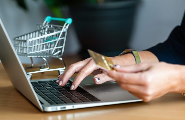 Mulher faz compra online segurando cartão de crédito