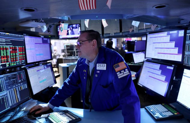 Trader em sala de pregão, focado em monitores com dados de mercado e gráficos financeiros.