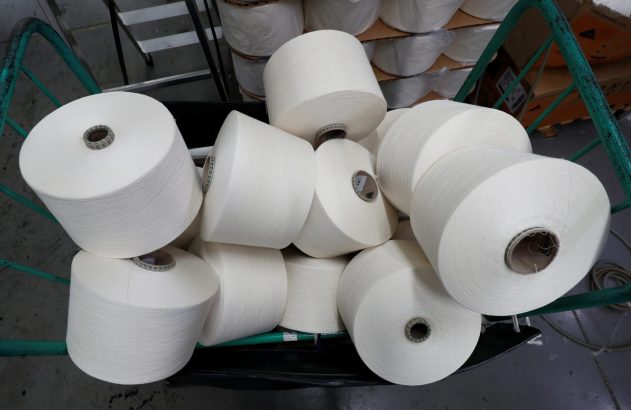 Cones de fio branco empilhados em um carrinho verde. Mais cones de fio são vistos empilhados no fundo.