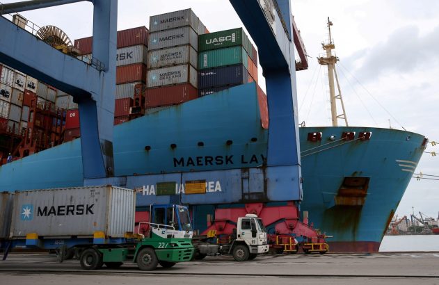 Navio cargueiro Maersk atracado em porto. Contêineres empilhados e veículos de carga operando na doca.