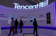 Pessoas observam displays da Tencent em estande de exposição, mostrando serviços digitais e IA.
