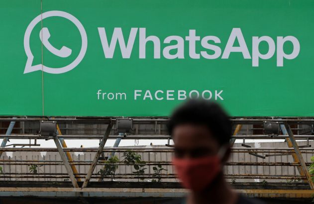 Outdoor verde com "WhatsApp from FACEBOOK". Pessoa de máscara vermelha desfocada em primeiro plano.