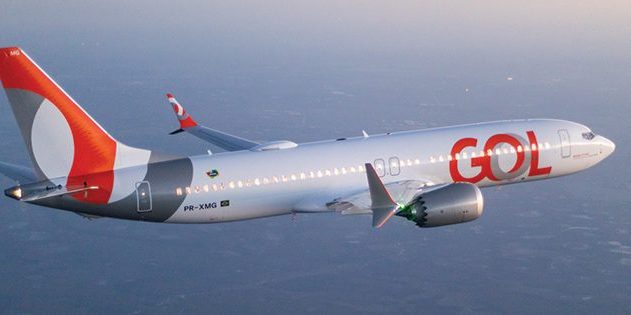 Avião da GOL em voo, visto de lado. Fuselagem branca com cauda laranja/cinza e logo GOL vermelho.