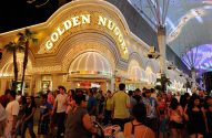 Fachada iluminada do Golden Nugget à noite, rua movimentada com pessoas caminhando e um grande teto luminoso.