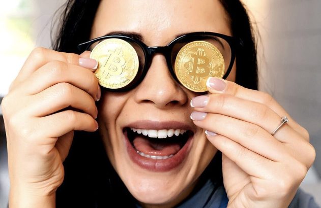 Mulher sorrindo, com moedas douradas de Bitcoin no lugar das lentes dos óculos, boca aberta.