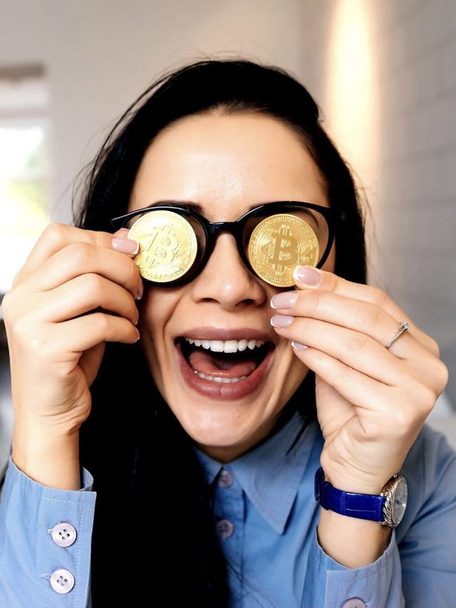 Mulher sorrindo, com moedas douradas de Bitcoin no lugar das lentes dos óculos, boca aberta.