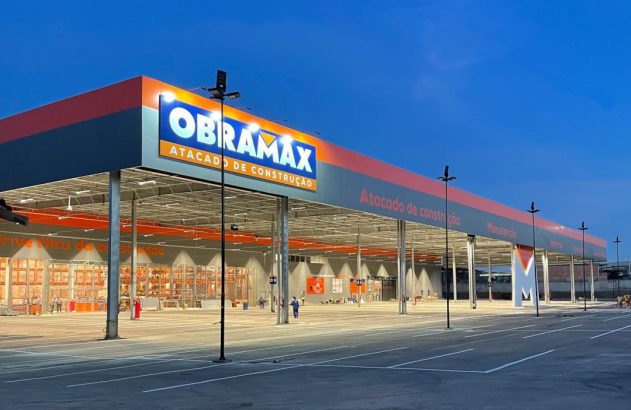 Loja atacadista de materiais de construção Obramax iluminada ao anoitecer, com amplo estacionamento.