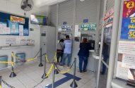 Interior de lotérica brasileira com clientes em guichês comprando bilhetes da Mega Sena e Quina, e pagando contas.