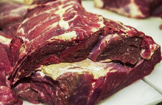 Vários grandes cortes de carne vermelha crua em uma superfície branca.