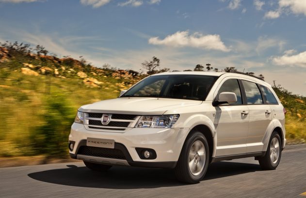 Fiat Freemont branco em movimento na estrada. Fundo borrado de paisagem e céu azul.