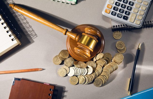 Martelo de juiz sobre moedas, calculadora e cadernos. Simboliza finanças legais, custos judiciais e justiça.