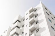 Edifício branco de arquitetura moderna, com janelas e varandas, sob céu claro.