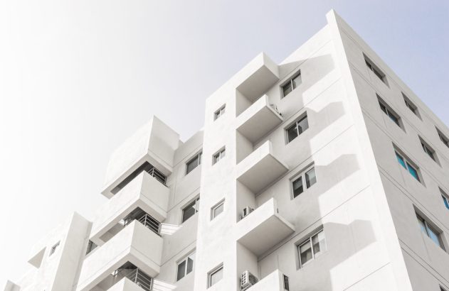 Edifício branco de arquitetura moderna, com janelas e varandas, sob céu claro.