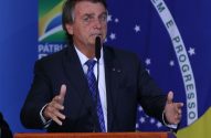 Jair Bolsonaro fala em um pódio, gesticulando com as mãos. Bandeira do Brasil com "PROGRESSO" visível ao fundo.