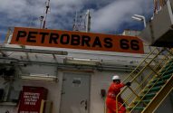 Funcionário de macacão laranja da Petrobras sobe escada. Sinal PETROBRAS 66 em ambiente industrial.
