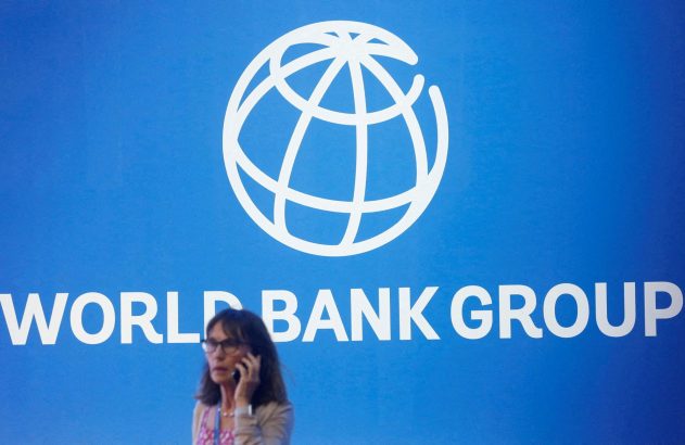 Mulher fala ao telefone em frente a um banner azul do World Bank Group com logo de globo.