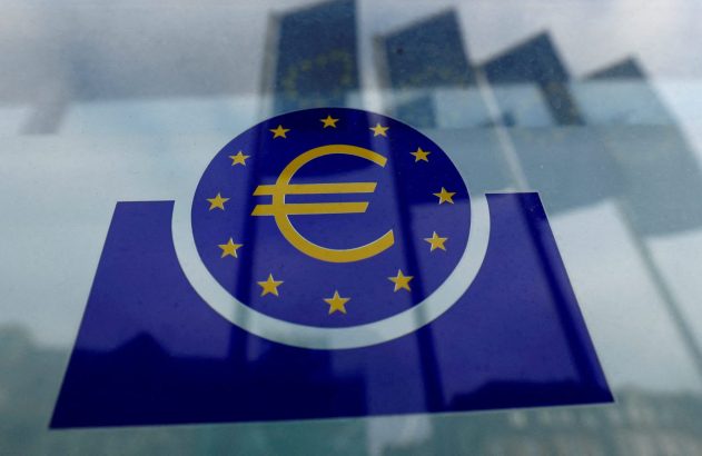 Logotipo do Euro (azul e amarelo) em adesivo no vidro. Reflexos de bandeiras desfocadas ao fundo.