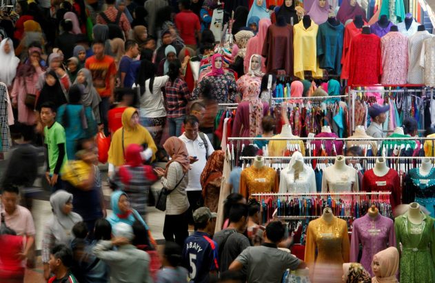 Loja ou mercado movimentado com pessoas, roupas em cabides e manequins exibindo trajes modestos.