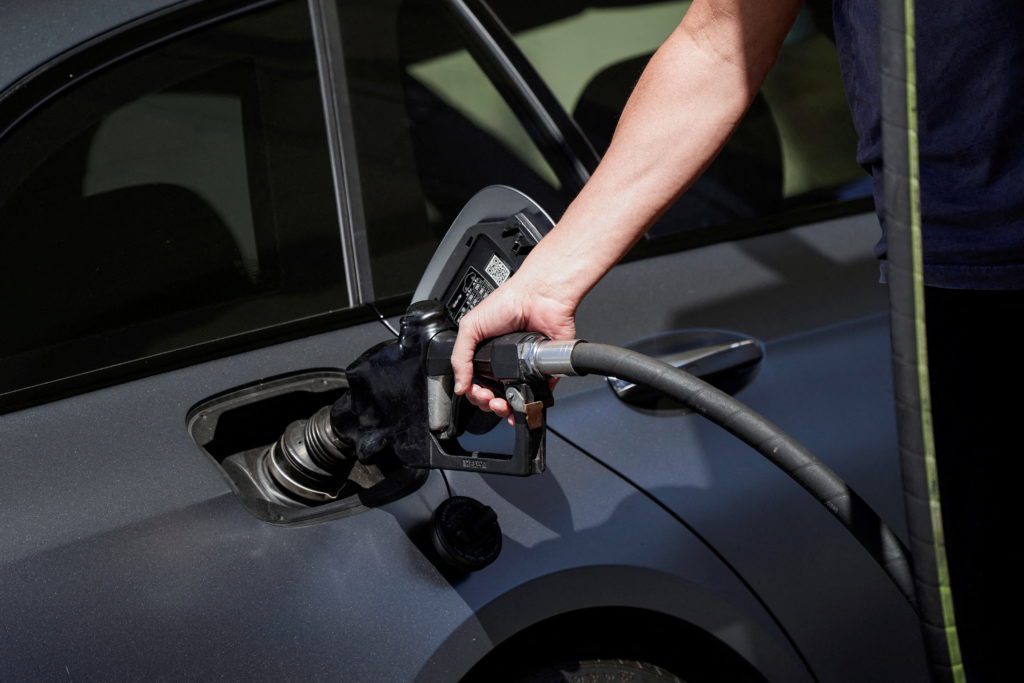 Mão inserindo conector de carregamento em carro elétrico cinza.