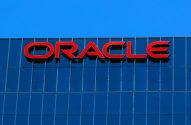 Logo vermelho ORACLE em edifício de vidro azul sob céu azul.