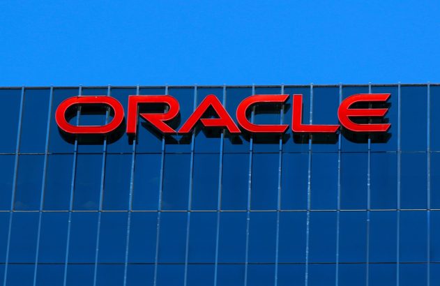 Logo vermelho ORACLE em edifício de vidro azul sob céu azul.