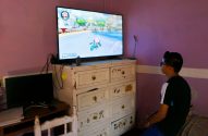 Jovem de costas jogando Mario Kart na TV em quarto roxo.