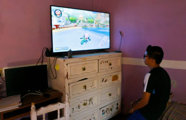 Jovem de costas jogando Mario Kart na TV em quarto roxo.
