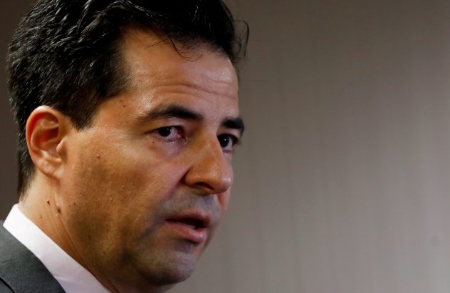 Close-up do rosto de um homem com boca entreaberta, olhando para o lado. Veste terno e camisa social.