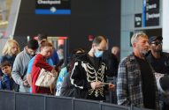 Pessoas em fila em um checkpoint de aeroporto. Um homem com máscara azul e moletom de esqueleto no centro.