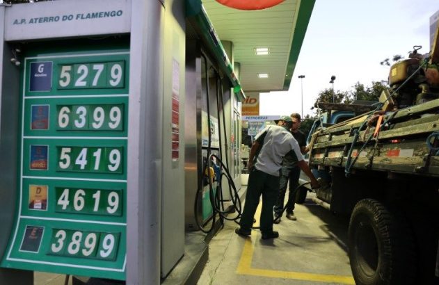 Frentista abastece caminhão em posto; painel com preços de gasolina, diesel e etanol.