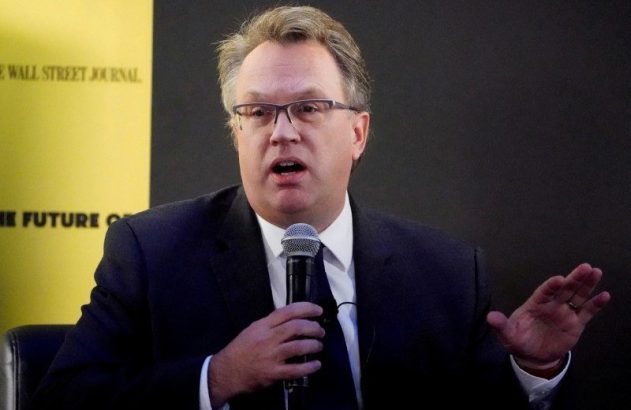 Homem de óculos e terno preto discursa em microfone, gesticulando. Banner do The Wall Street Journal ao fundo.