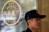Homem de boné em frente ao logo em caracteres chineses do Banco Central, em porta de vidro.