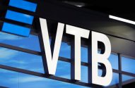 Letreiro VTB branco e iluminado. Fundo azul com barras e luzes retangulares azuis.