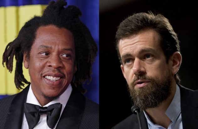 Jay-Z sorri ao lado de Jack Dorsey barbudo, que parece falar em um microfone.