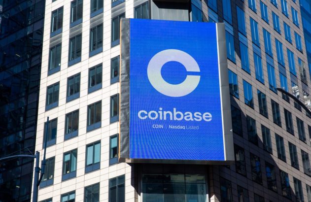 Um letreiro digital grande da Coinbase com seu logo 'C' e nome, junto a 'COIN Nasdaq Listed', em um edifício urbano.